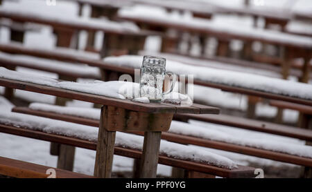 Snow-covered benches and tables in the 'Hirschgarten' beer garden. There is an empty beer mug on a table. Stock Photo