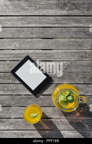 E-reader and a glass of fruit drink on a wooden table. Stock Photo