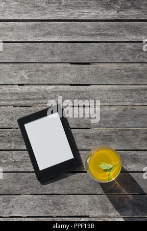 E-reader and a glass of fruit drink on a wooden table. Stock Photo