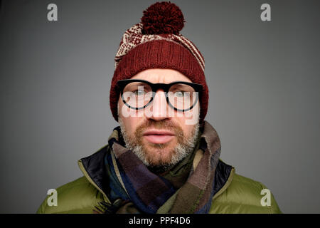 Close up portrait of middle aged europeam man in funny warm hat and glasses noticing hidden camera. Stock Photo