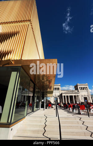 Guests on the terrace of the museum restaurant 'Ella' in front of the extension of the Lenbachhaus with its shining golden facade. In the background the Propylaea on Koenigsplatz. Stock Photo