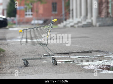 Grocery trolley stands alone on the street on the wet asphalt Stock Photo