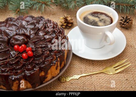 Chocolate cake decorated with bunch of viburnum, cup of coffee on table with branch of spruce, fork and sackcloth.