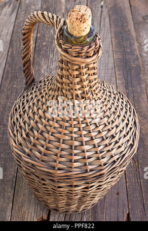 Old demijohn wicker wrapped glass bottle on old  wooden table Stock Photo