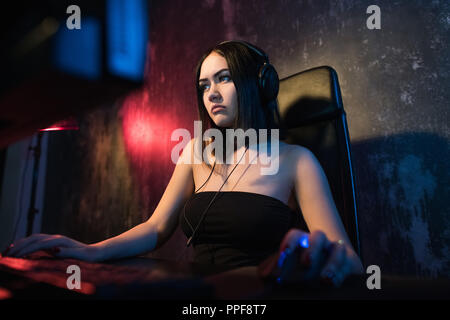 Beautiful Friendly Pro Gamer Girl Does Video Game Gameplay stream, Wearing Headset Talks and Chats with Her Fans and Team into Headphones Microphone. Teenagers Having Fun. Background Neon Retro Colors. Stock Photo