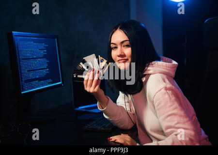 Closeup of young female theift in sweatshirt with hood transfering money from bills of stolen creding cards Stock Photo