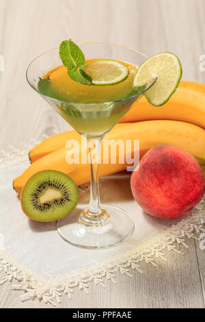 Kiwi jelly with lime pieces in the glass topped mint leaves, nectarine, kiwi and banana on the white napkin Stock Photo
