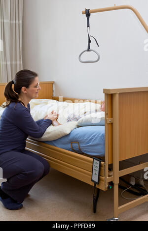 Woman at the nursing bed of her terminally ill grandmother, holding her hand and talking to her. Concept of dying at home or in a hospice. Stock Photo