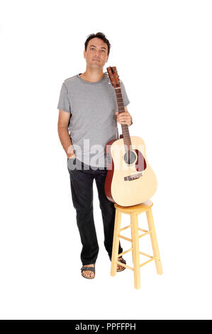 A young handsome man taking a brake from playing the guitar, standing in jeans gray shirt, sandals, isolated for white background Stock Photo