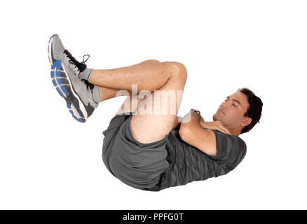 A handsome tall man lying on the floor with his arms crossed over his chest doing stomach chrunshes, isolated for white background Stock Photo