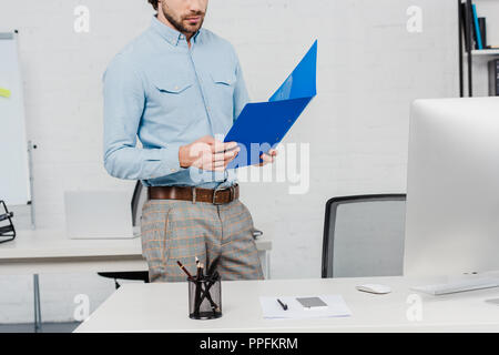 cropped shot of young businessman reading documents in folder at modern office