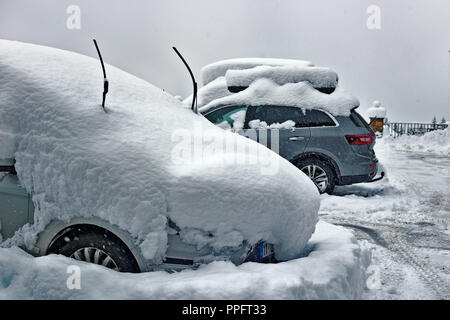 Cars on the parking in snow. Cloudy winter day, snowfall, snowdrifts on roofs of cars. Near traces from tires on snow Stock Photo