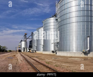 bright shinny metal grain elevators next to railroad tracks Stock Photo