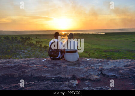 Two young people sit on the rocks at Ubirr Lookout to watch the sunset Kakadu National Park, Northern Territory, Top End, Australia Stock Photo