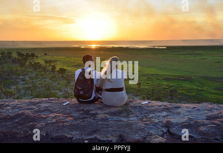 Two young people sit on the rocks at Ubirr Lookout to watch the sunset Kakadu National Park, Northern Territory, Top End, Australia Stock Photo