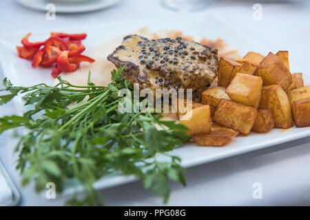 Closeup detail of beef fillet steak in pepper sauce at luxury restaurant with outdoor rable setting Stock Photo