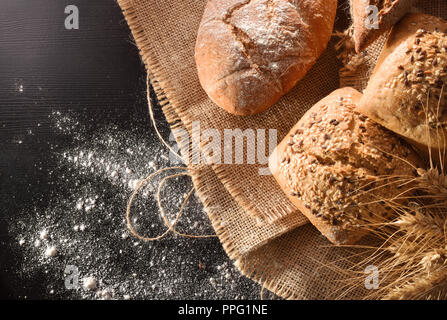 Assortment of bread on sackcloth and flour on black table. Top view. Horizontal composition Stock Photo