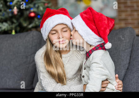 cute little boy in santa hat kissing sister at christmas time Stock Photo