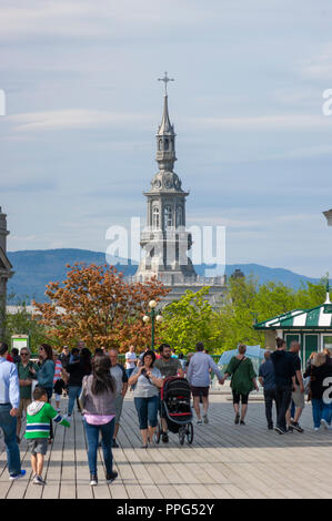 Tourists enjoying a stroll on the Dufferin Terrace. The ornamental steeple of the Camille-Roy Building (Séminaire de Québec) can be seen in the back. Stock Photo