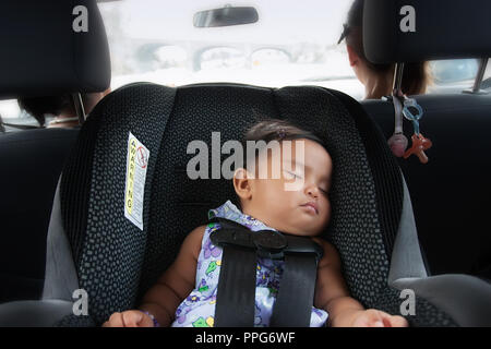 Latino baby girl sleeping safely in her carseat, in moving car with two females in the front Stock Photo