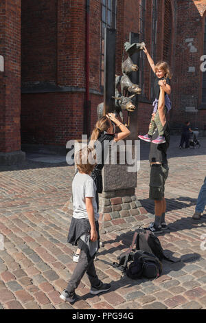 A father and daughter pose for a photo while visiting the famous Bremen Town Musicians sculpture in the medieval center of Old Riga, Latvia. Stock Photo