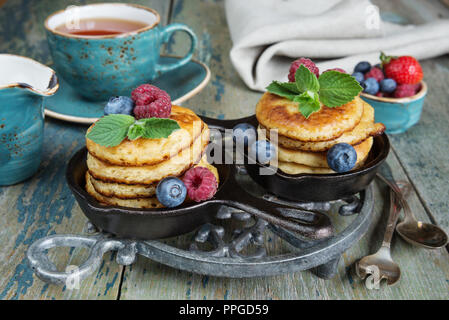 Breakfast of pancakes in cast-iron frying pans, fresh berries and black tea, in rustic style Stock Photo