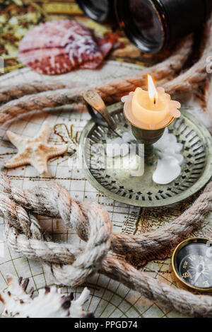Time for adventures. Antique candlestick with a burning candle, vintage compass, binoculars and rope with knot are on old world map Stock Photo
