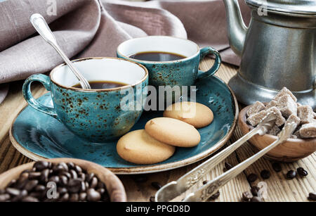 Two blue vintage cups of black coffee, biscuit cookies and antique pewter coffee pot  surrounded by linen cloth, sugar pieces and coffee beans on old 
