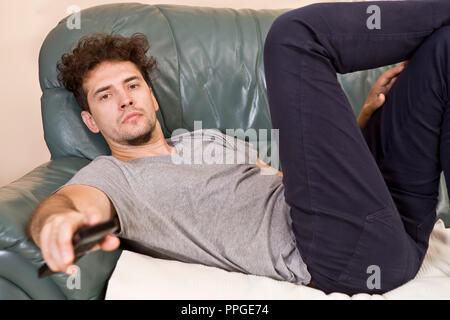 A young man watches television and changes channels while relaxing Stock Photo