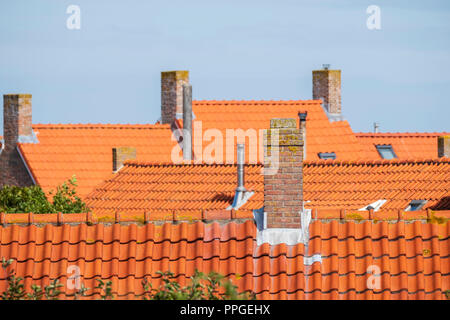 stone chimneys on the roofs with orange roof tiles against a blue sky in an old neighborhood Stock Photo