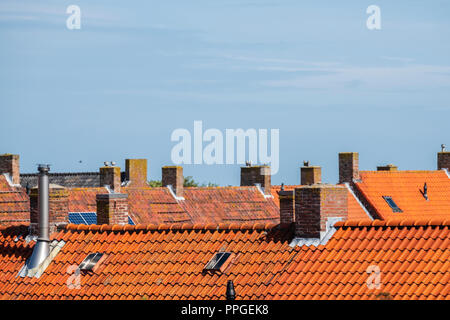 stone chimneys on the roofs with orange roof tiles against a blue sky in an old neighborhood Stock Photo
