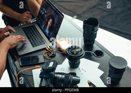 Photographer looking at photos after a photo shoot on a laptop. Photographer editing photos on laptop with camera and lens placed on table. Stock Photo