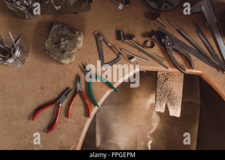 Top view jewelry maker workbench with tools on table. Equipment and tools of a goldsmith on wooden working desk inside a workshop. Stock Photo