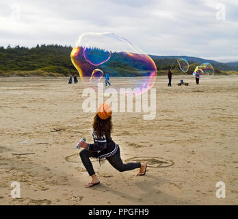 A young woman tries to keep a large soap bubble in the air at a a bubble blowing festival on the beach near Yachats, Oregon. Stock Photo