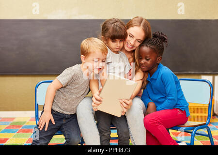 Kids and caregivers using tablet pc online have fun with social media in kindergarten Stock Photo
