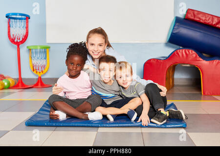 Three children and their kindergarten teacher sit together in the gym in kindergarten Stock Photo