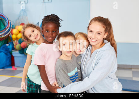 Kindergarten teacher and group of multicultural children as friends hold together Stock Photo