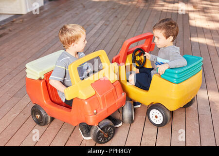 Two boys ride a pedal car in the garden of the daycare or kindergarten Stock Photo