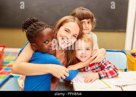 Young woman as a childminder or teacher hugs children in daycare or elementary school Stock Photo