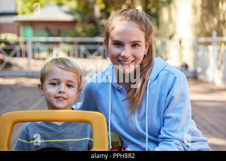 Woman as a childminder or kindergarten teacher together with a boy in a pedal car Stock Photo