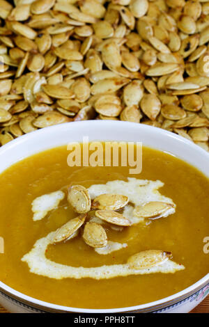 Close up view of bowl of pumpkin soup with toasted spiced pumpkin seeds in the background Stock Photo