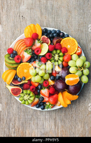 Healthy fruit platter, strawberries raspberries oranges plums apples kiwis grapes blueberries on the dark grey wooden table, vertical, top view, copy  Stock Photo