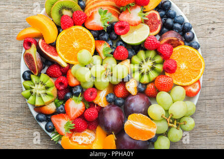 Healthy fruit platter, strawberries raspberries oranges plums apples kiwis grapes blueberries on the dark grey wooden table, top view, close up Stock Photo