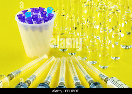 Syringes, needles in measuring glass and ampoules on yellow background. Stock Photo