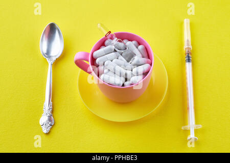 Pink cup with capsules and ampoule. Spoon, syringe on yellow background Stock Photo