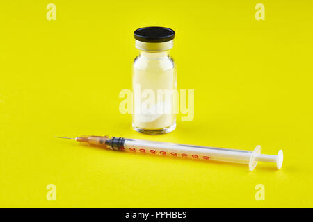 Small sealed bottle with medicine and syringe on yellow background. Stock Photo
