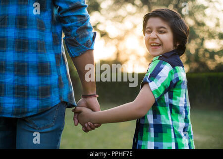 Rear view of a smiling boy holding hand of his father standing in park. Stock Photo