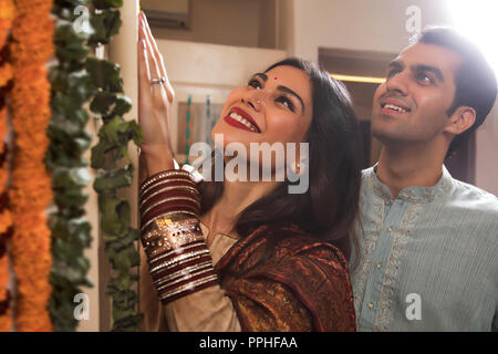 Close up of happy young couple in traditional dress decorating their home with flowers. Stock Photo