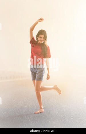 Young woman dancing joyfully on the road against foggy background. Stock Photo