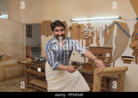 Happy carpenter hitting a nail with hammer in his workshop. Stock Photo